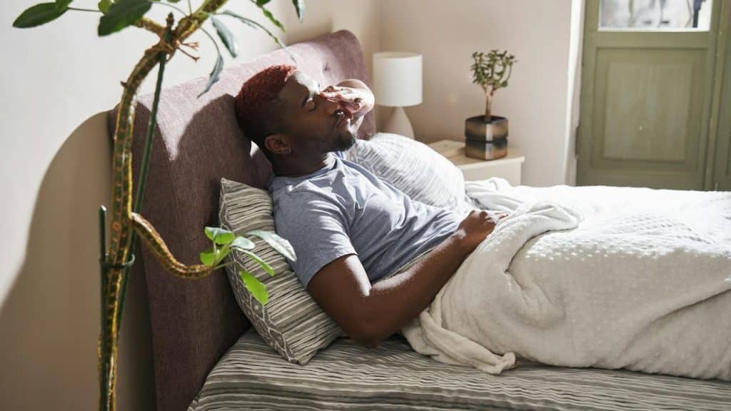 A man lying in bed covering his face.