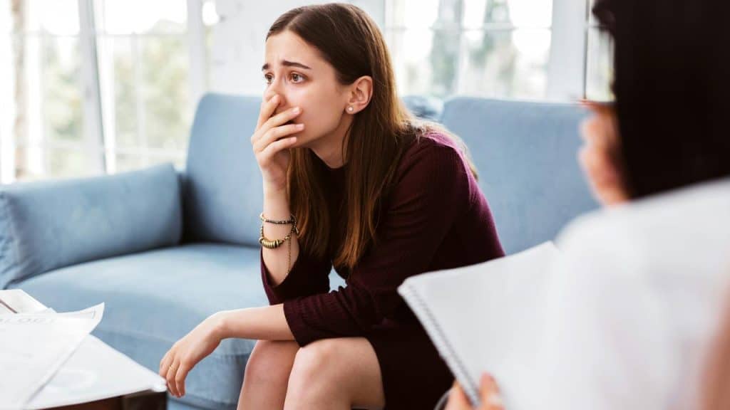 A woman sitting on a couch looking distressed during a conversation.