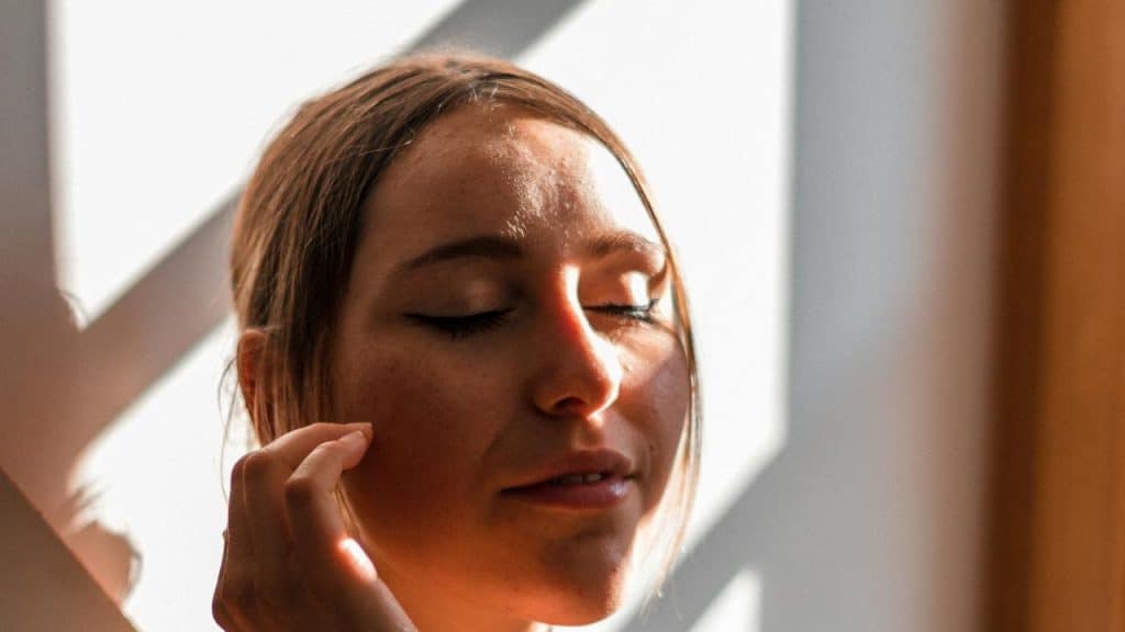 A woman with closed eyes standing in sunlight.