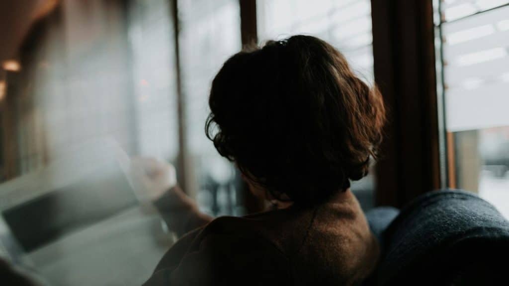 A person sitting by a window reading a newspaper.