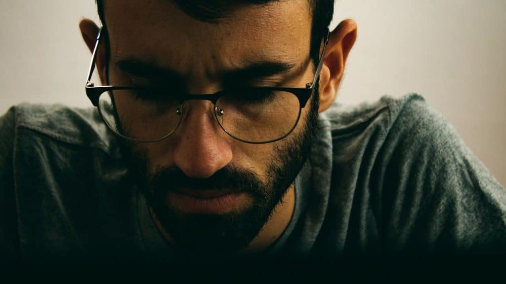 A man wearing glasses looking down with a serious expression.