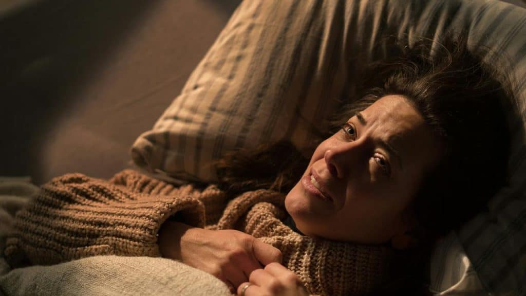 A woman lies in bed looking emotional.