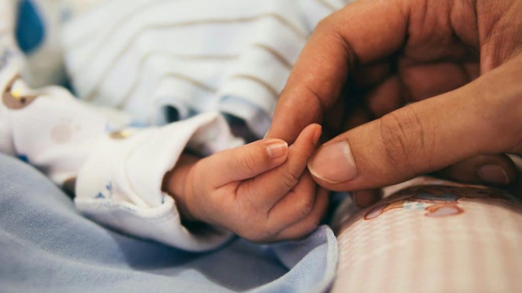 A baby holds an adult's finger.