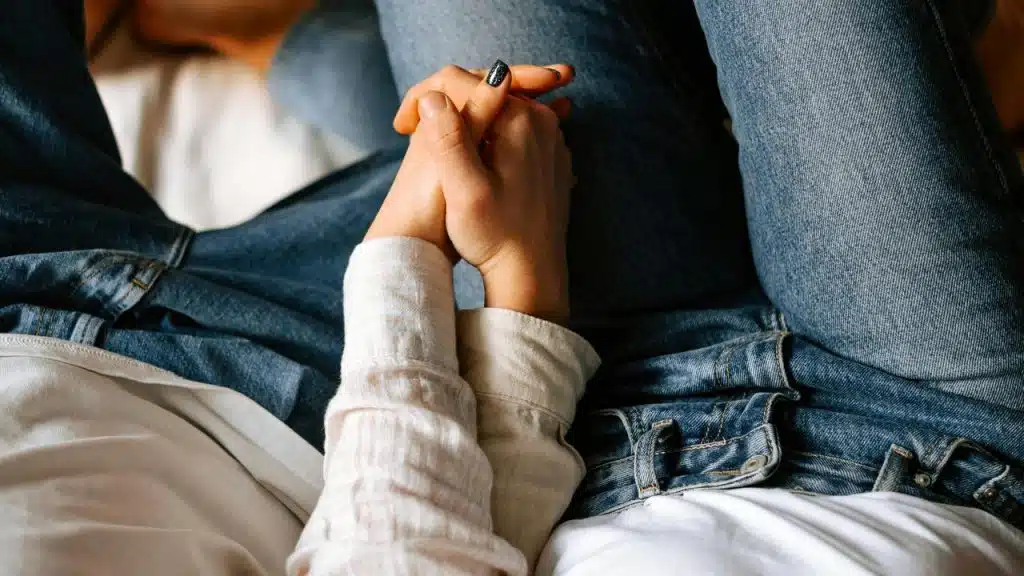 A couple holds hands while sitting close together in jeans.