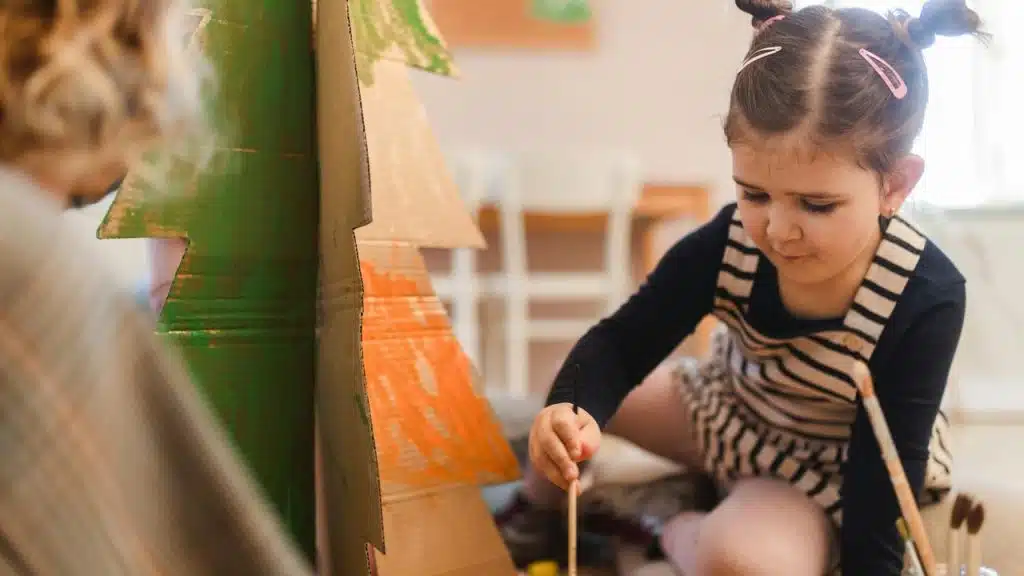 A young girl paints a cardboard tree.