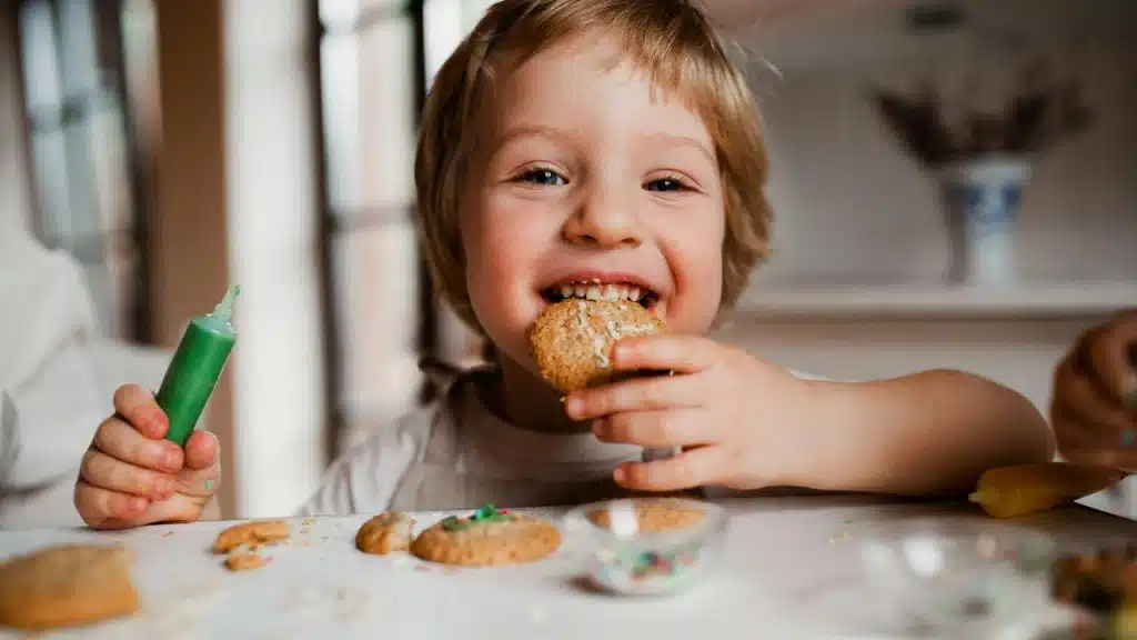 A young child smiles while eating a cookie.