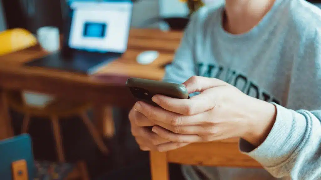 A person holds a smartphone while sitting at a desk.