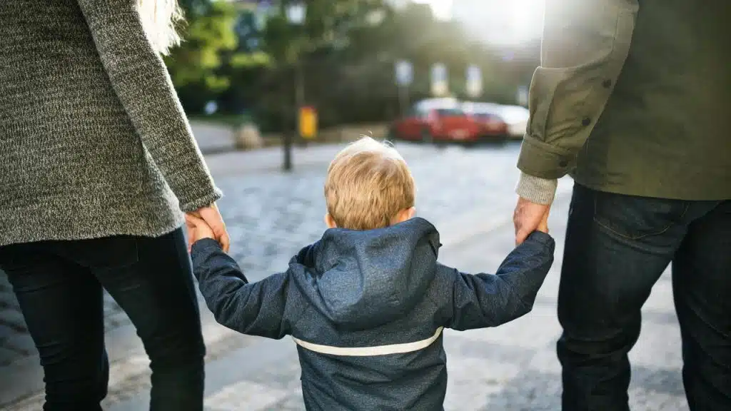 A child walks while holding hands with two adults.