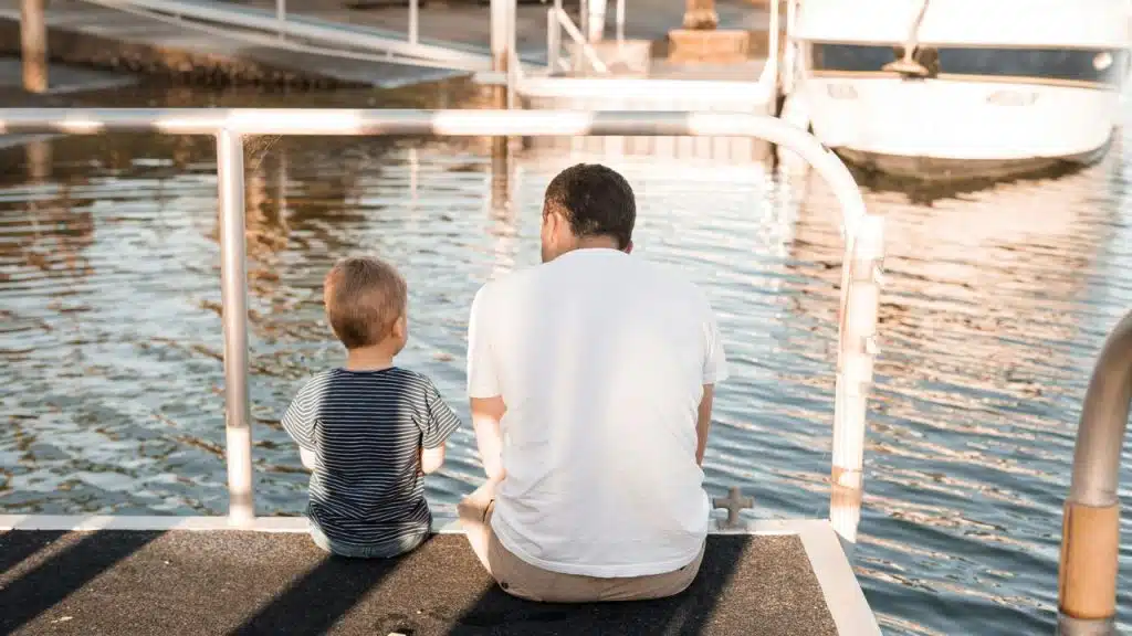 A man and a child sit together by the water.