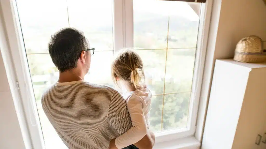 A man holds a child while looking out a window.