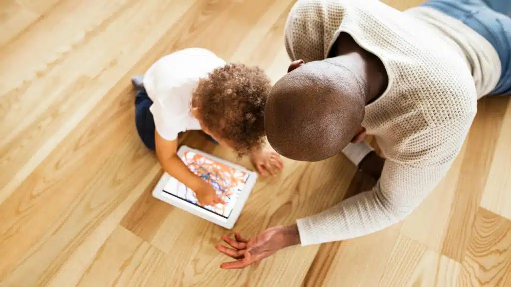A man and a child draw on a tablet while sitting on the floor.