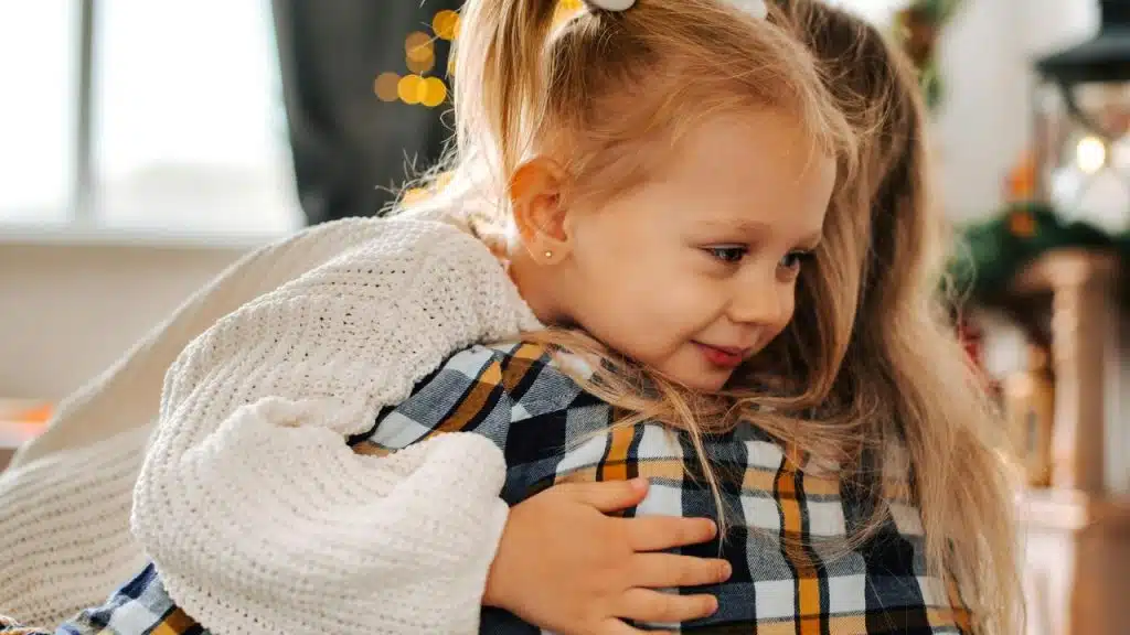 A young girl hugs someone while smiling.