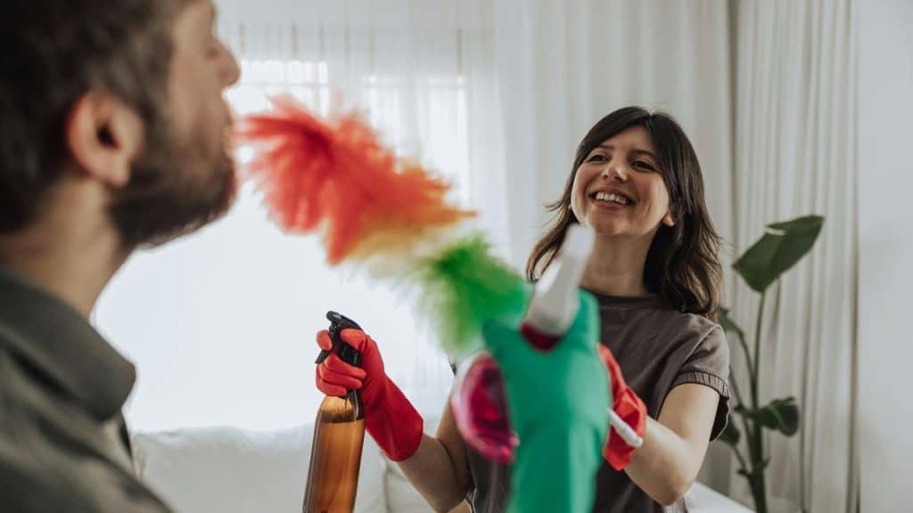 A couple laughing while cleaning together at home.