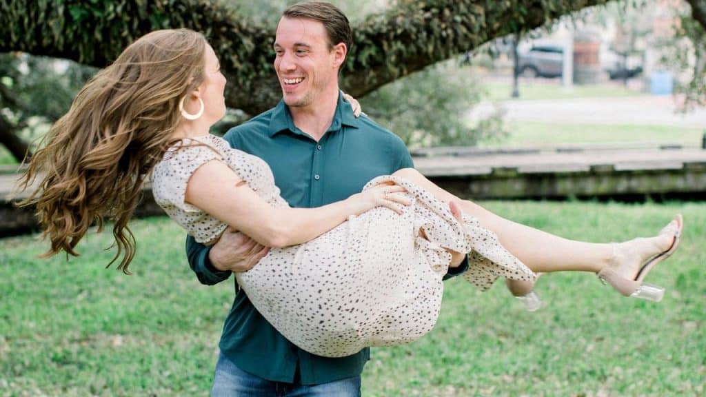 A man happily carrying a woman in his arms outdoors.