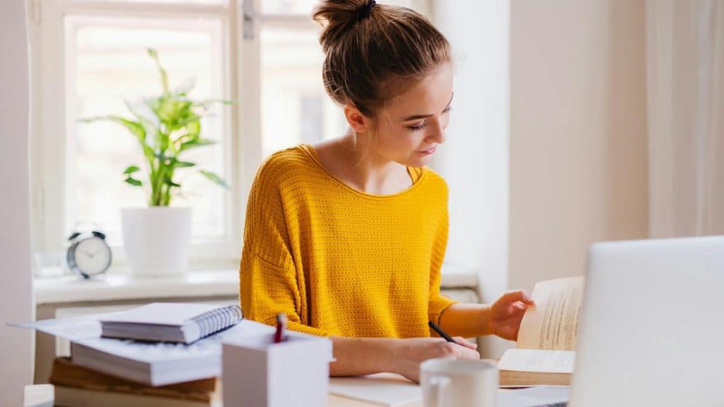 A woman studying at a desk with books and a laptop.