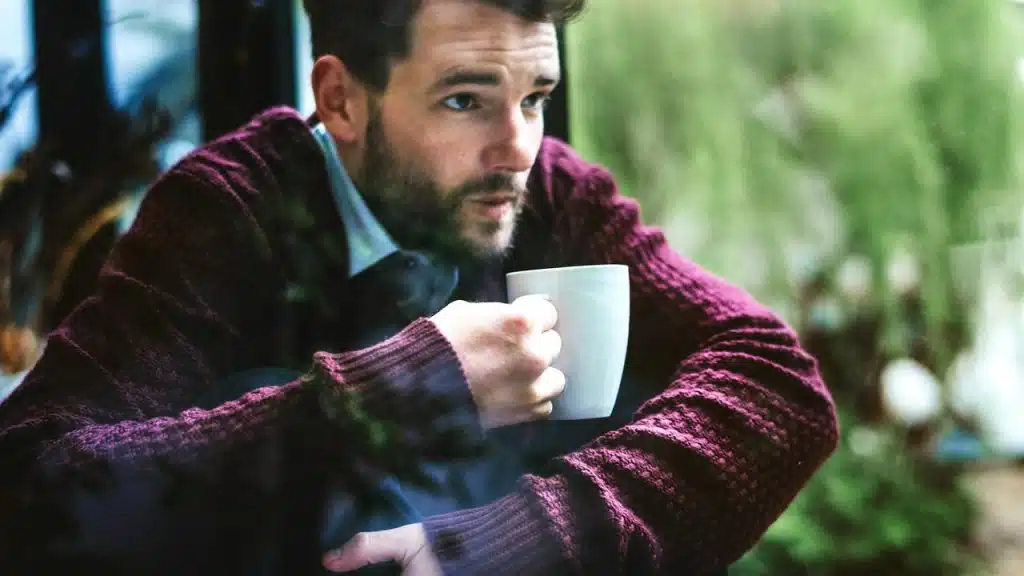 A man holding a coffee cup looking outside.