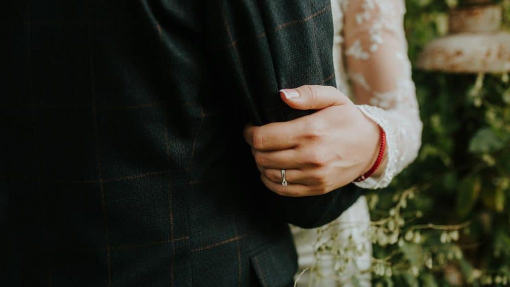 A close-up of a person wearing a ring holding onto someone's arm in formal attire.