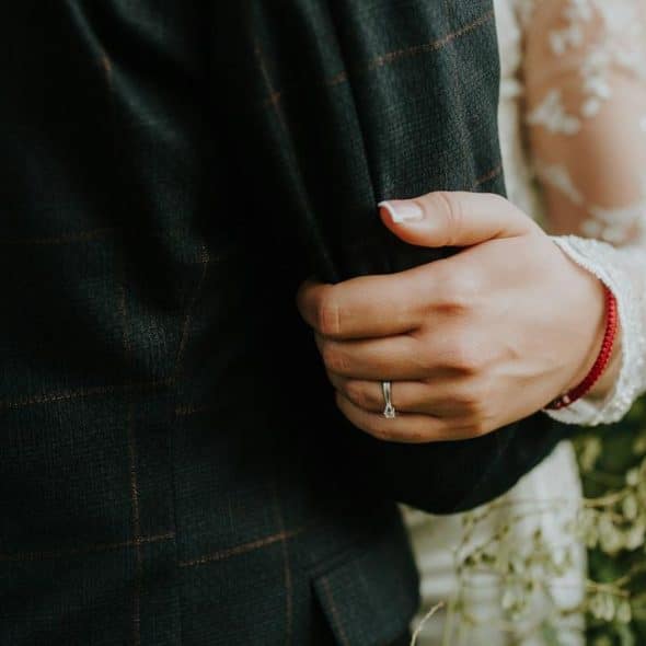 A close-up of a person wearing a ring holding onto someone's arm in formal attire.