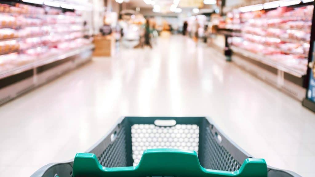 A shopping cart in the aisle of a brightly lit supermarket.
