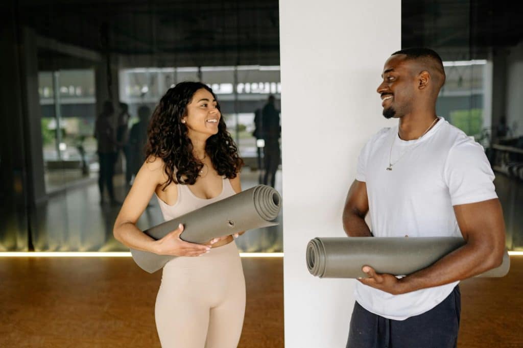 A man and woman holding a gray yoga mat 