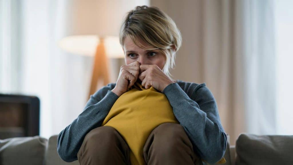 A person sitting on a couch holding a pillow with a worried expression.