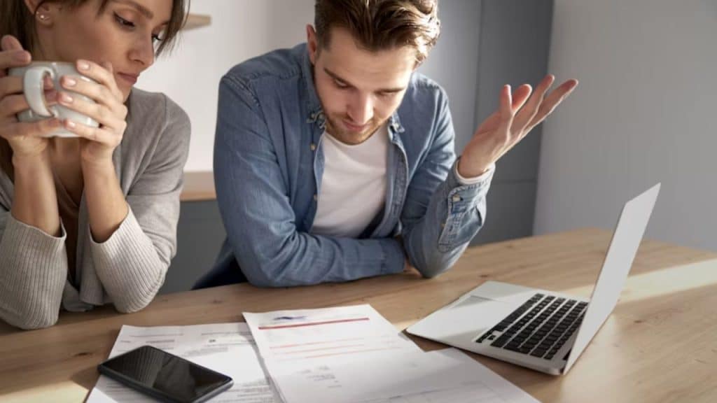 Man reviewing bills while his partner looks stressed