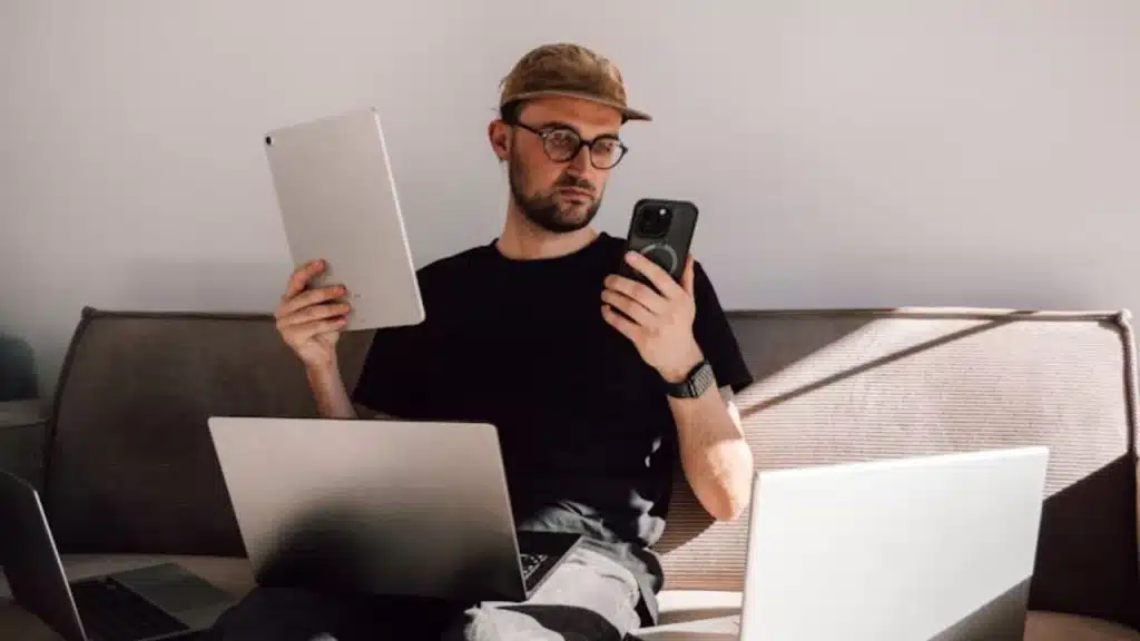 Workaholic man surrounded with laptops and holding a phone and a tab