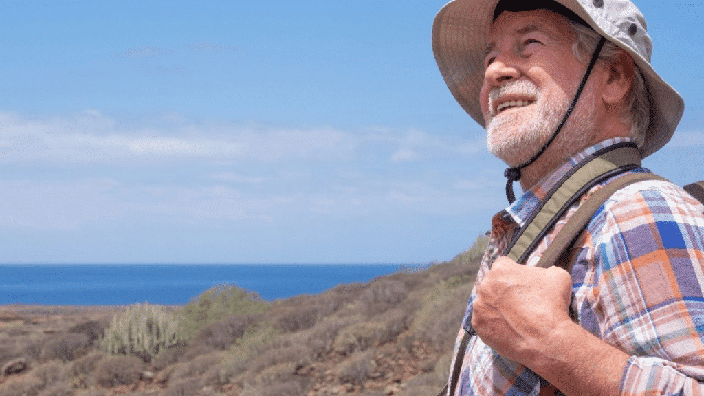 A happy, older man with a beard and a sun hat smiles while looking at the ocean.