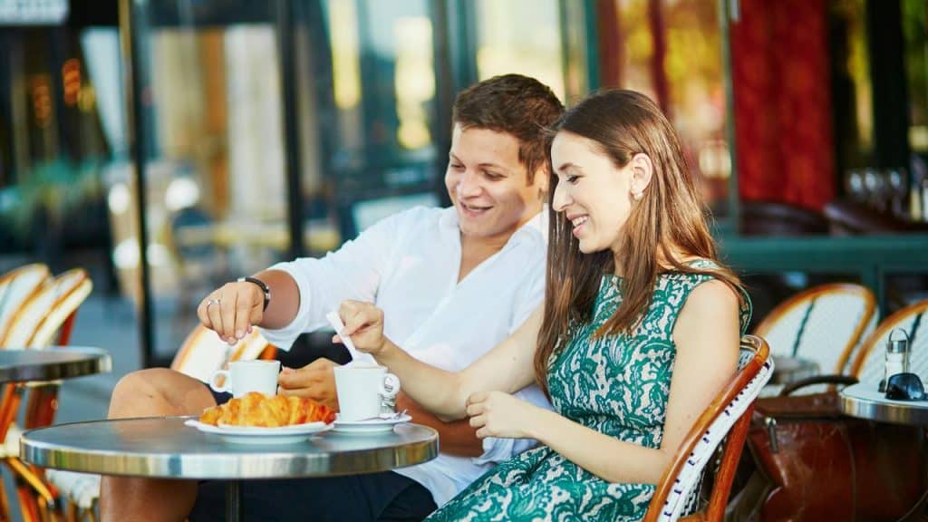 A couple sitting at a café table enjoying coffee and croissants.