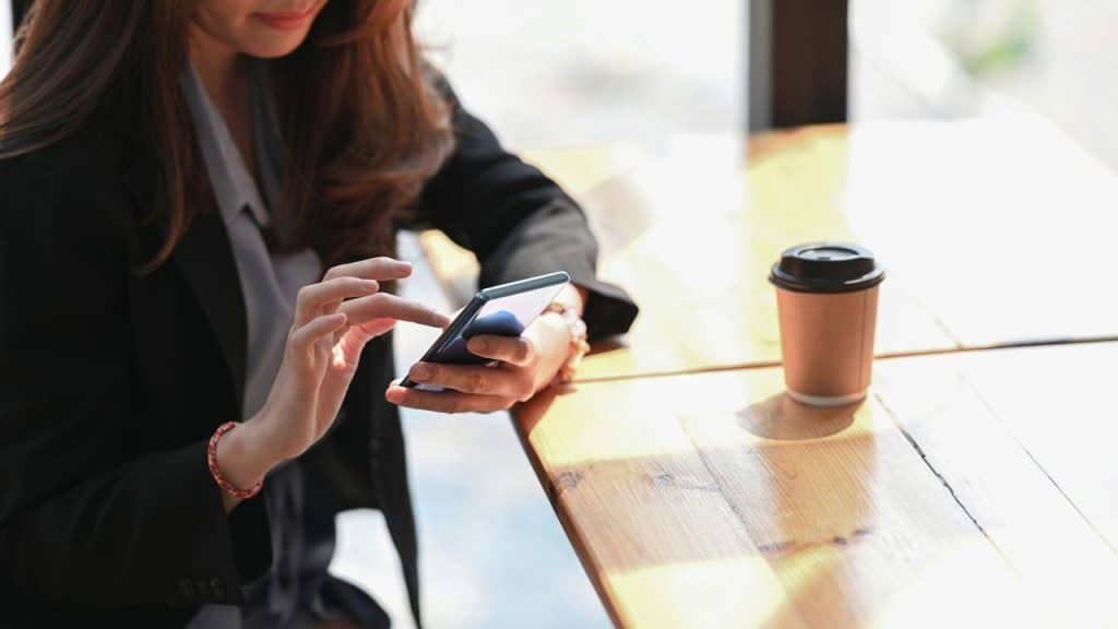 A woman using a smartphone at a café table with a coffee cup.