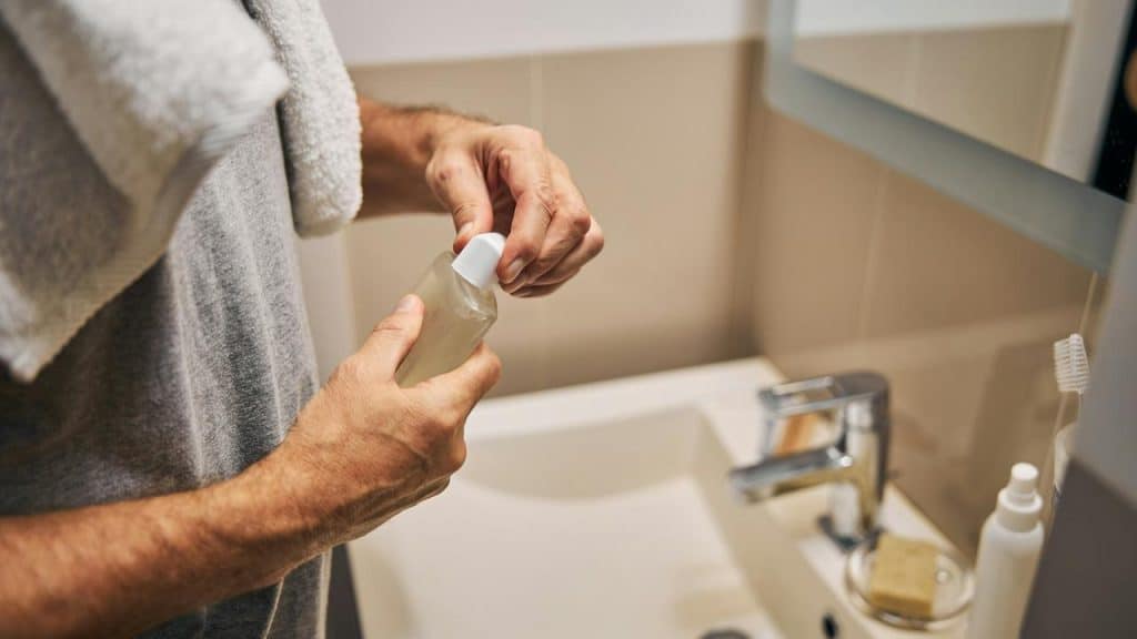 A man in a bathroom opening a bottle of liquid soap or lotion.
