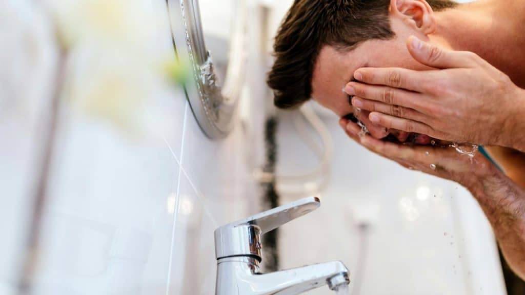 A man washing his face at a sink.