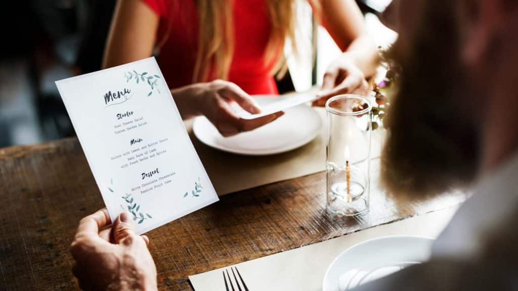 A person holding a restaurant menu at a candlelit table.