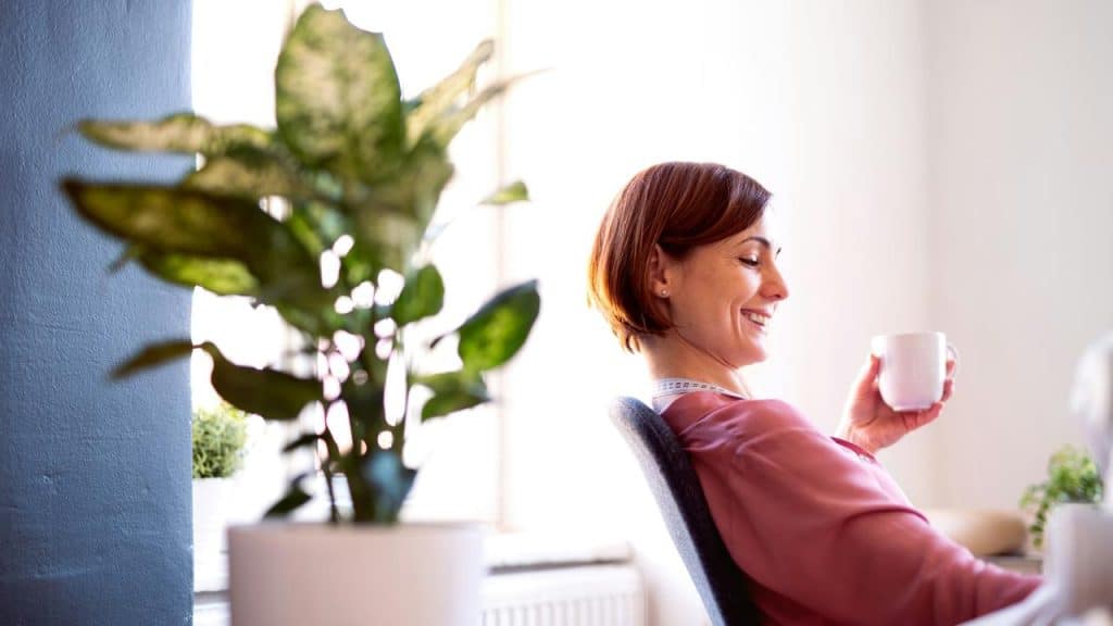 A woman sits smiling with a cup in hand, enjoying a moment of relaxation.