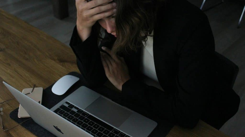 A woman sitting at a desk with a laptop, holding her head in frustration.