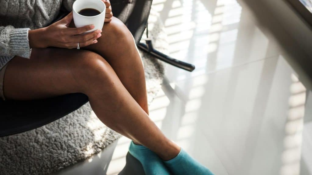 A person sitting with crossed legs holding a cup of coffee.
