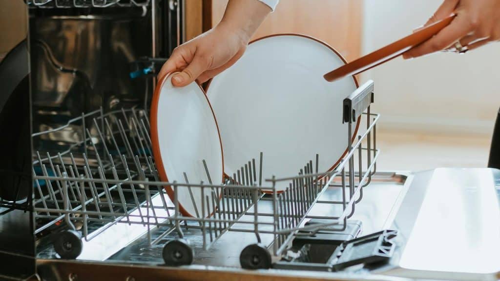 A person loads white plates into a dishwasher.