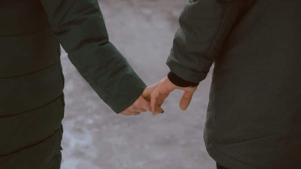 A couple holds hands while walking outdoors in winter jackets.