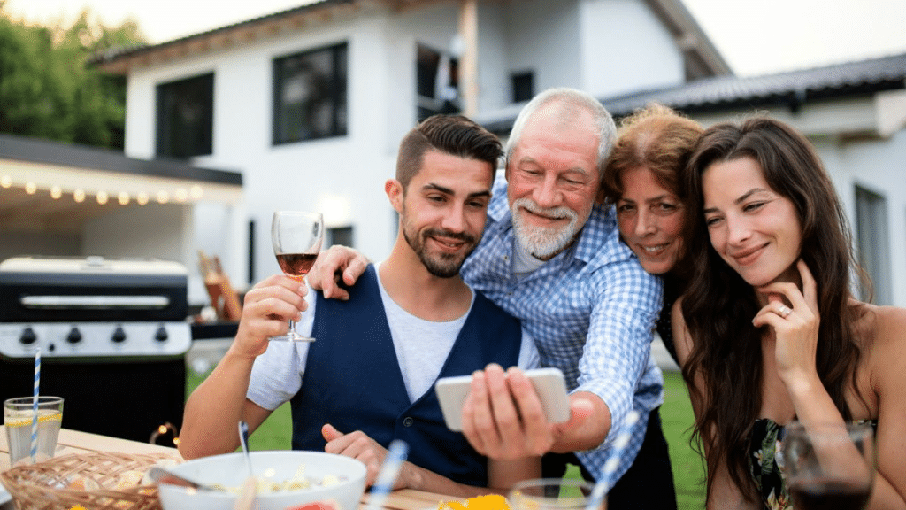A smiling family is gathered around a table outdoors, looking at a phone.