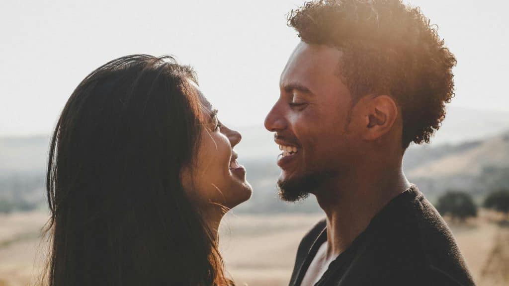 A couple smiles at each other closely while standing outdoors.