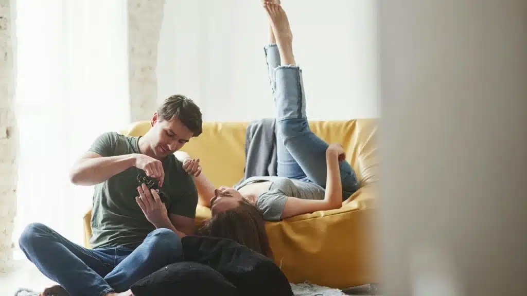 A man and woman recline on a couch, focused on a digital camera.