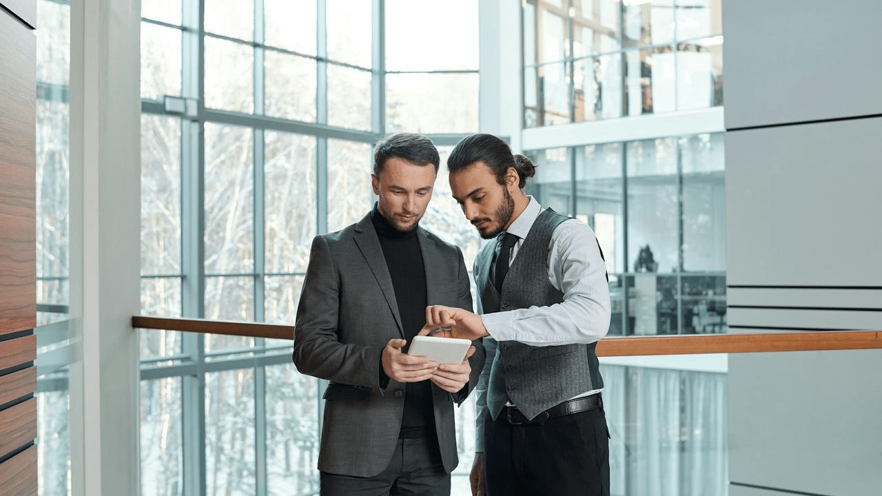 A pair of businessmen looking at a tablet in a modern office building.