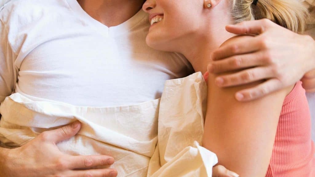 A couple smilingly embraces each other in bed.