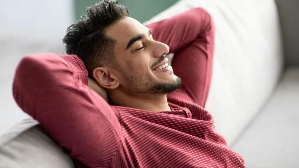 A man with his hands on the back of his head and casually relaxing on the couch.