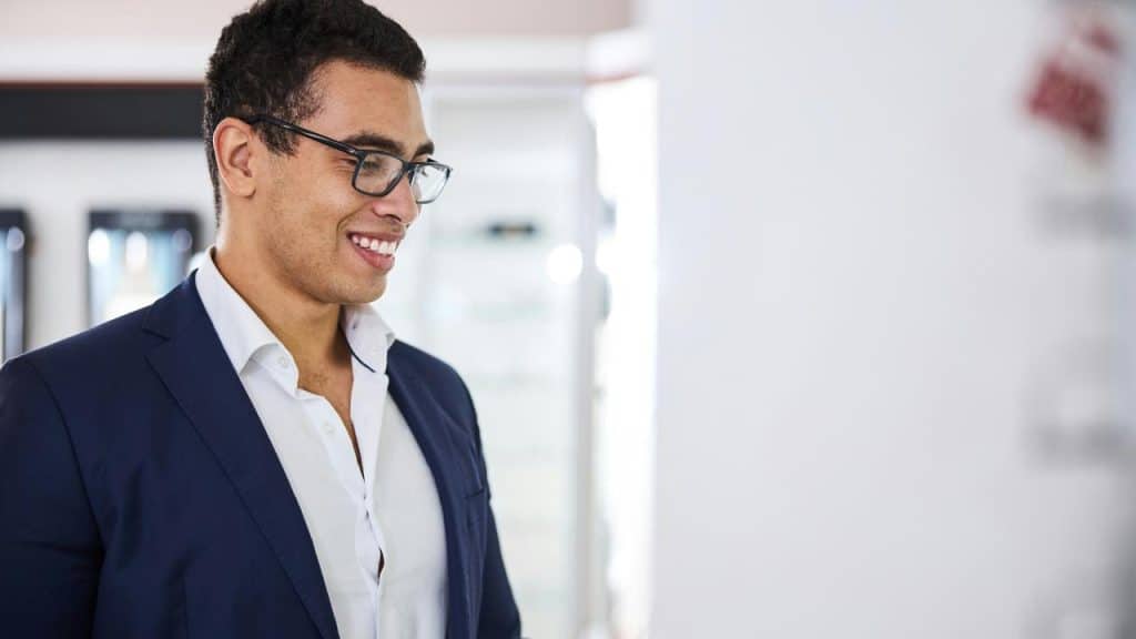 A man with glasses smiling and glancing at something.