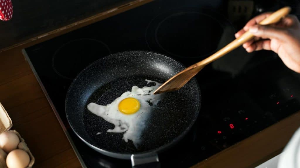 A person frying an egg in a pan on a stovetop.
