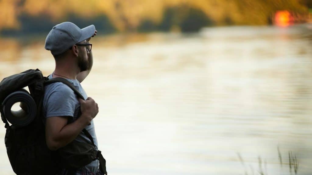 A man with a backpack standing by a river.