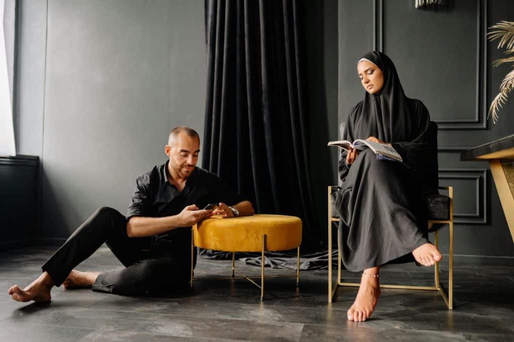 A man using his smartphone on the floor while a woman reads a book.