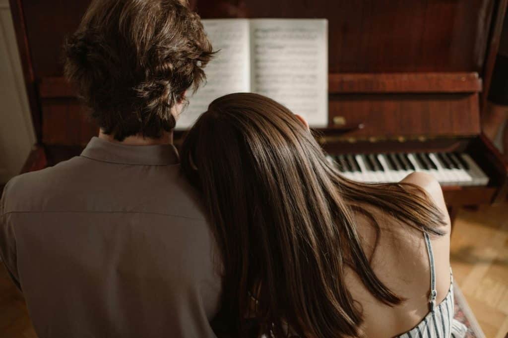 A man watching a woman playing piano