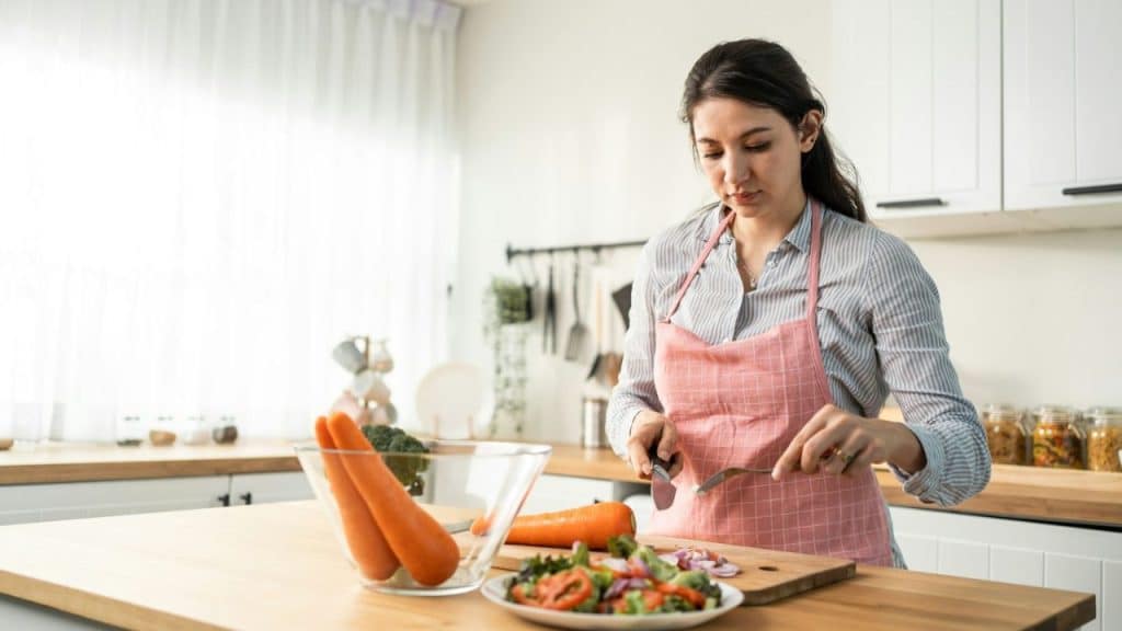 A woman in an apron is chopping vegetables on a cutting board in a kitchen.